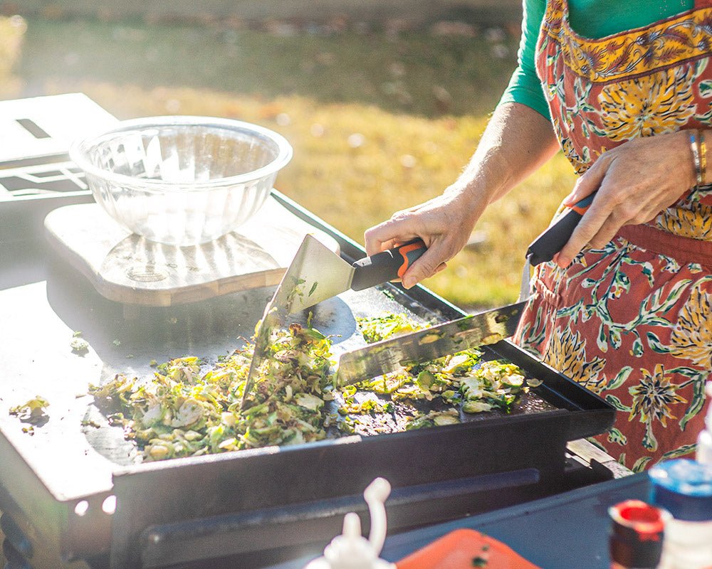 Woman cooking on the griddle with two spatulas.