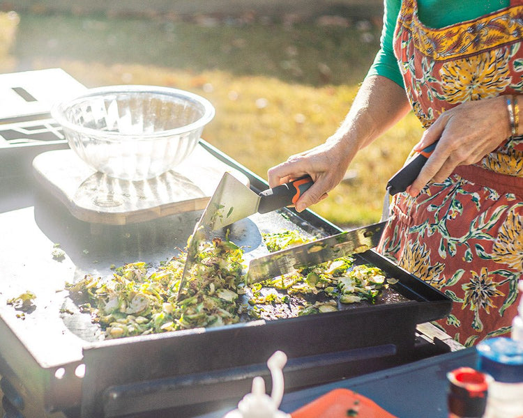 Woman cooking on the griddle with two spatulas. 
